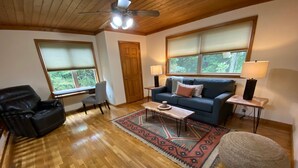 A living room with a wooden ceiling, a blue sofa, a black leather chair, a small table, and a patterned rug.