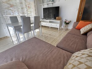 A modern living room with a sofa, a dining table with chairs, a TV, and a white cabinet. - APARTBEACH - SANTA ELENA AIR-CONDITIONED AND NEXT TO THE BEACH (Salou)