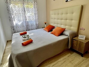 A neatly made bed with a headboard, a tray with cups and a rolled towel, and a small wooden nightstand with a sign. - APARTBEACH - SANTA ELENA AIR-CONDITIONED AND NEXT TO THE BEACH (Salou)