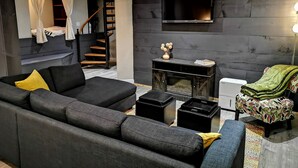 A modern living room with a sofa, a coffee table, a fireplace, a television, and a staircase. - 3 BR Harp Hygge House. Only 8min to Hidden Valley! (Huntsville)