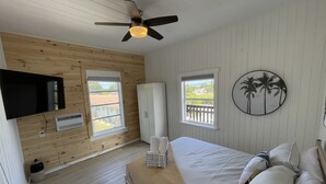 Ein Schlafzimmer mit einem Bett, einem Deckenventilator, einem an der Wand montierten Fernseher und zwei Fenstern.