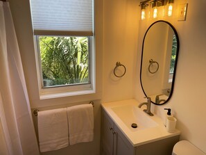 A bathroom with a window, a sink, a mirror, and a toilet.