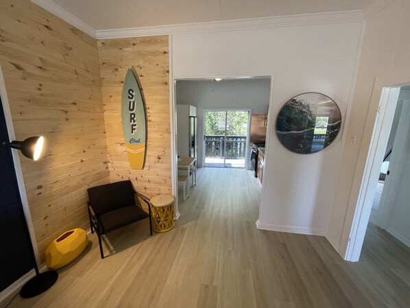 A hallway with a wooden wall, a surfboard sign, a round mirror, and a dining area with a table and chairs.