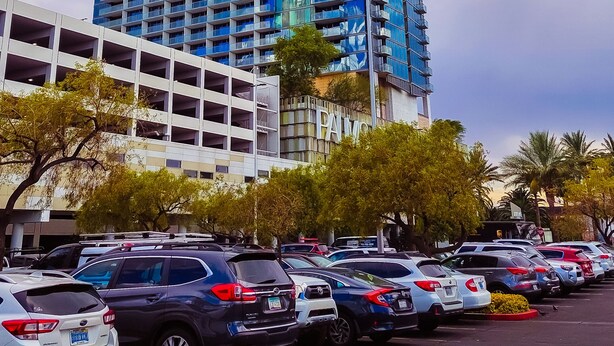 Ein hohes Gebäude mit blauer Fassade, umgeben von einem Parkplatz mit verschiedenen Autos.