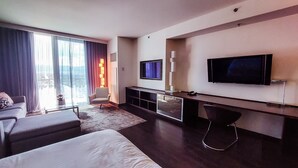 Ein modernes Hotelzimmer mit einem großen Bett, einem Fernseher, einer Sitzecke und einem Balkon mit Vorhängen.