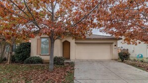 A single-story house with a beige exterior, a front garage, and a tree with autumn leaves.