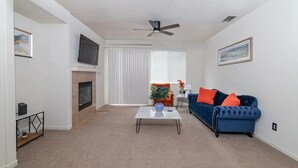 A living room with a fireplace, a blue sofa, a coffee table, and a ceiling fan.
