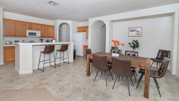 A modern kitchen with white cabinetry, a central island, and a dining area with a wooden table and chairs.