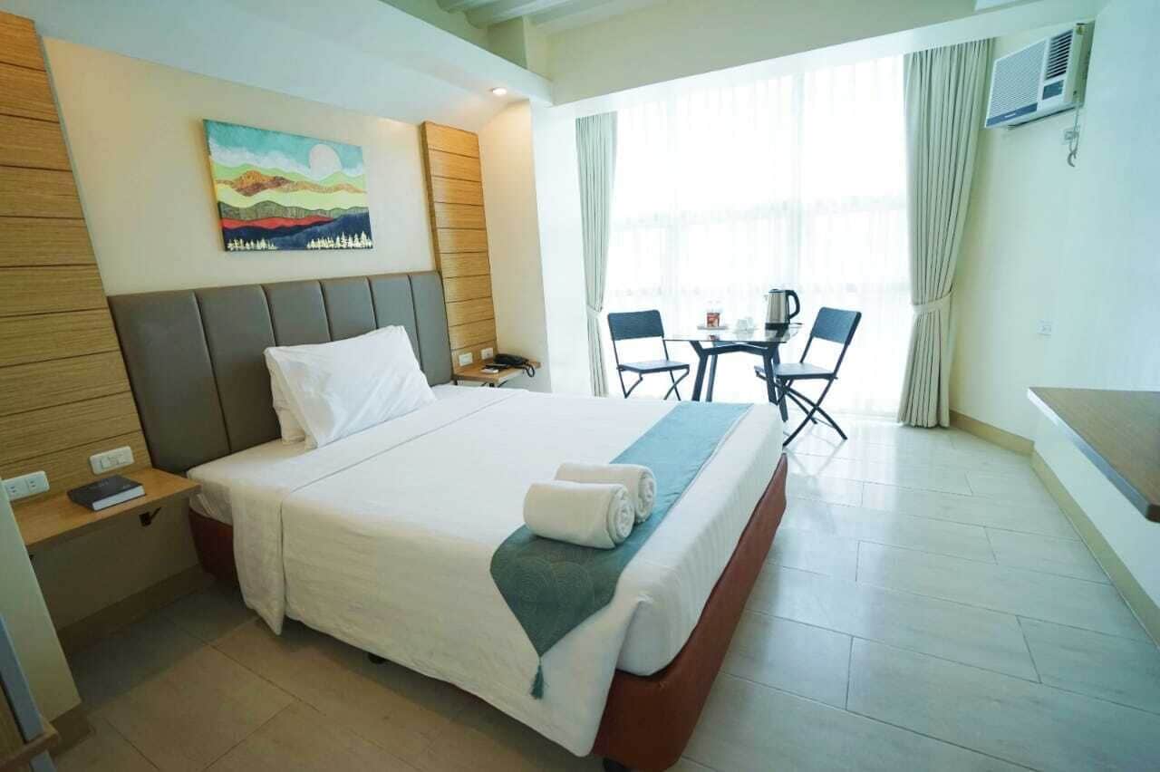 A hotel room with a large bed, a desk with a chair, a small table with chairs, and a painting on the wall.