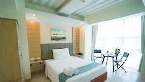 A hotel room with a bed, bedside table, a painting on the wall, a desk with a chair, and a window with curtains. - Chambre Hotel Mactan (Lapu-Lapu)