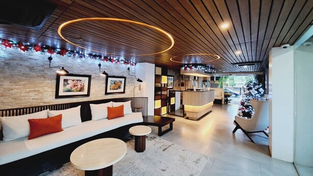 A modern lounge area with a wooden ceiling, a sofa with red cushions, a round coffee table, and a reception desk. - Chambre Hotel Mactan (Lapu-Lapu)