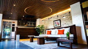 A modern living area with a wooden ceiling, a brick wall, a white sofa with orange cushions, and a coffee table. - Chambre Hotel Mactan (Lapu-Lapu)