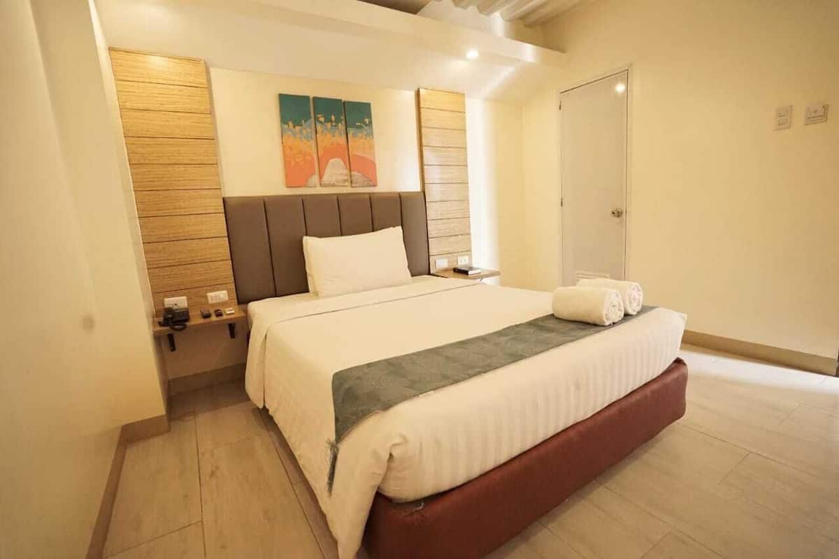Una habitación de hotel moderna con una cama grande, una mesita de noche, una obra de arte en la pared y una puerta.