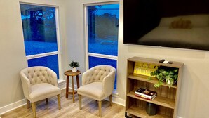 Un salon avec deux fauteuils, une petite table d’appoint, une bibliothèque et un téléviseur fixé au mur.