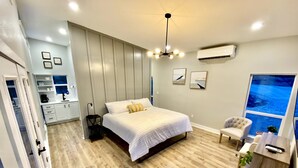 Une chambre moderne avec un grand lit, une table de chevet, une chaise et une vue sur la mer par la fenêtre.