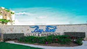 Schild für Bay Front Villas & Apartments mit einer Steinmauer und einem angelegten Garten.
