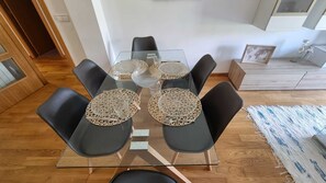 Un tavolo da pranzo con sedie nere, piano in vetro trasparente e sottopiatti intrecciati.