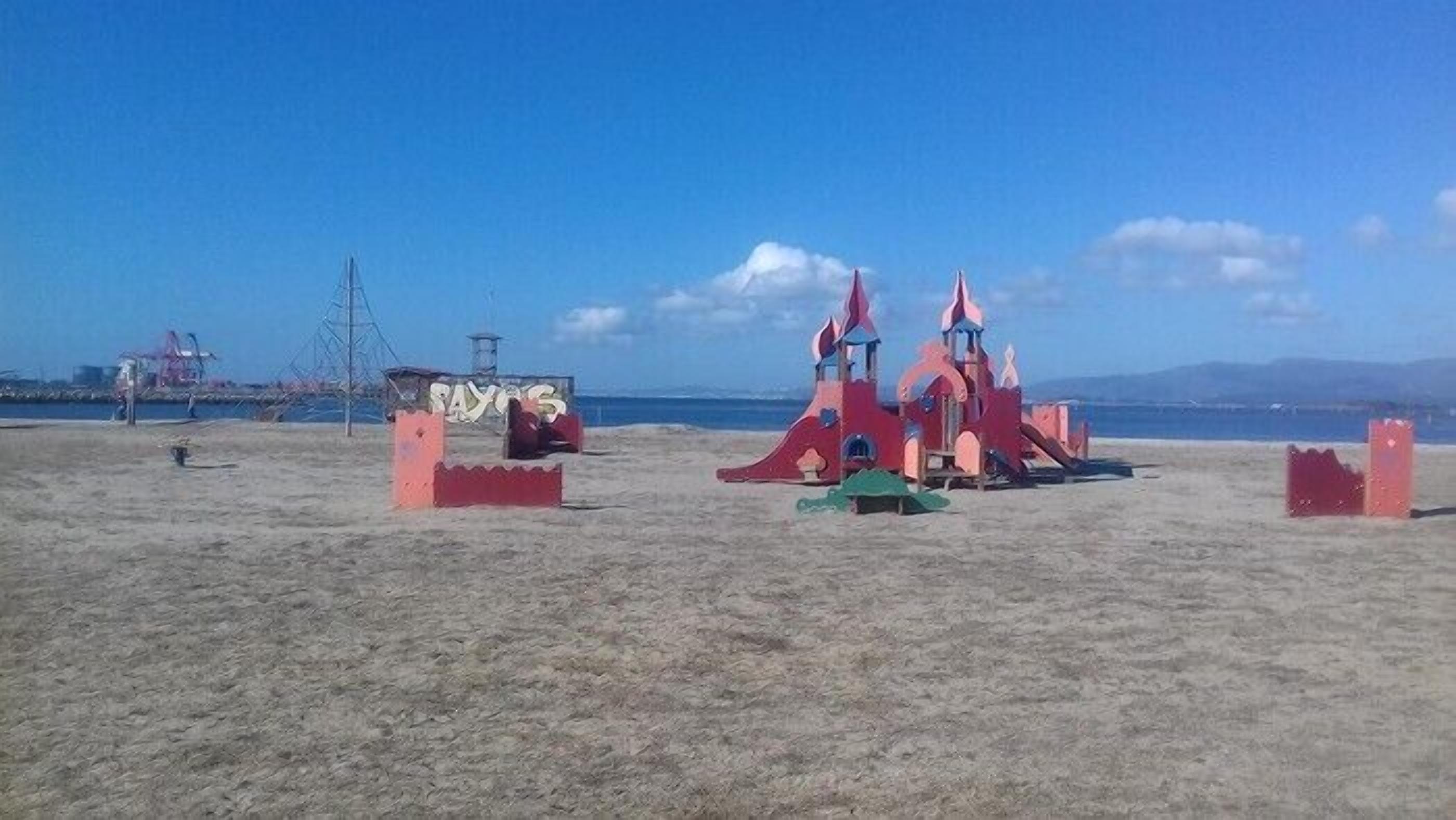 A beach with a large red play structure and a smaller green play area.