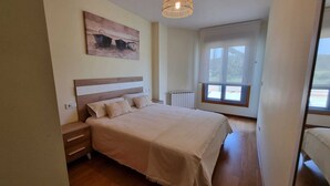 A bedroom with a large bed, a nightstand, a bedside table, a radiator, and a window with a view of the outside.