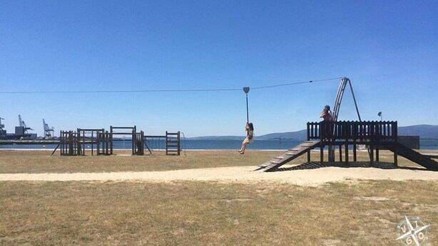 A playground with swings and climbing structures near a beach.
