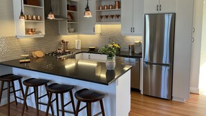 A modern kitchen with white cabinetry, a stainless steel refrigerator, and a central island with bar stools.