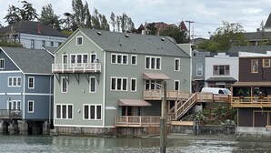 A waterfront property with a multi-story house featuring balconies, a wooden deck, and a small boat docked nearby.