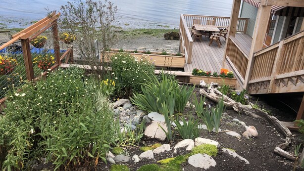 A wooden deck with a table and chairs, overlooking a calm lake with boats and a distant shoreline.