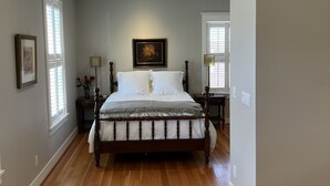 A bedroom with a wooden floor, a large bed, a nightstand, a lamp, and a painting on the wall.