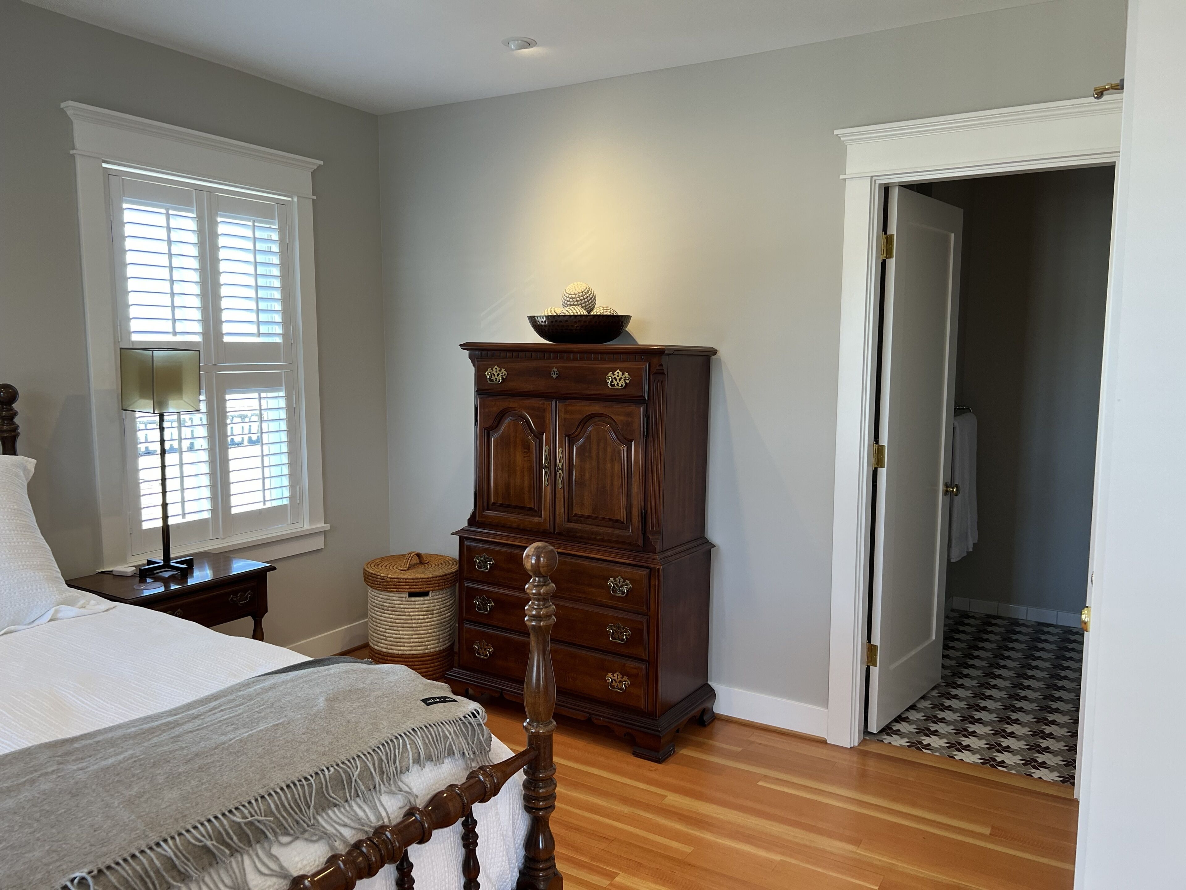 A bedroom with a bed, a dresser, a lamp, and a window with blinds.
