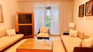 Une chambre d’hôtel avec un canapé, un lit, une télévision, une table basse en verre et une vue sur la verdure.