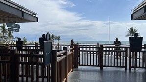 Un balcon en bois donnant sur l’océan, une enseigne indiquant l’arrêt de bus « Estacion Beachland », et un pot de fleurs.