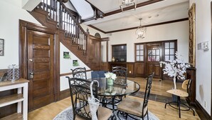 A spacious dining area with a round glass table, black metal chairs, and a wooden staircase leading to an upper level. -  White House at Grand Central (St. Louis)