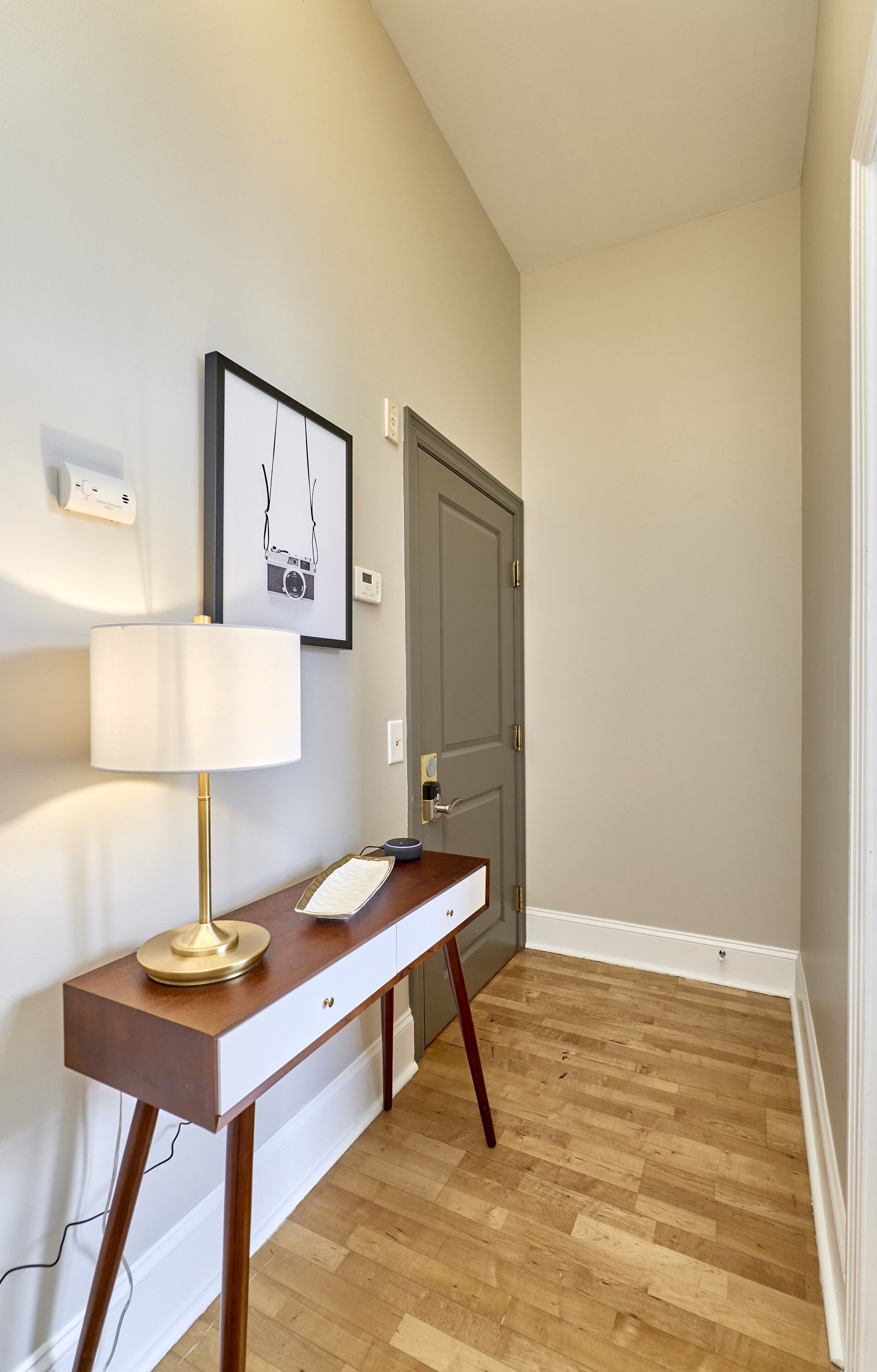 A hallway with a desk, lamp, framed picture, and a door.