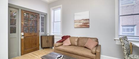 A living room with a brown leather sofa, a wooden coffee table, a patterned rug, and a window with blinds.
