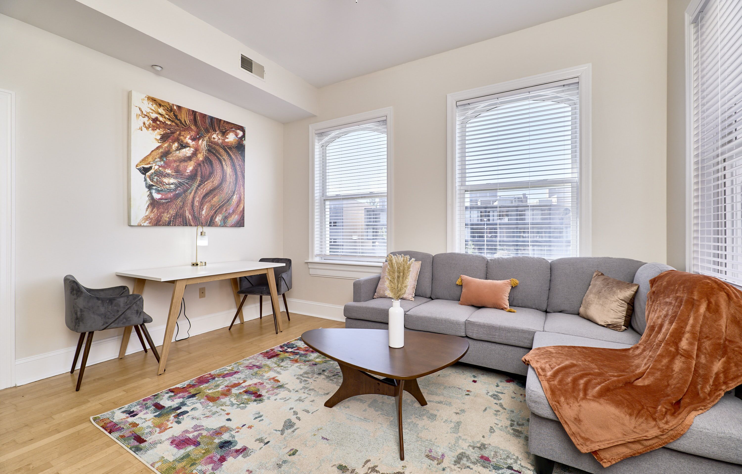 Een moderne woonkamer met een grijze bank, een bijzettafeltje, een bureau en een kleurrijk vloerkleed.