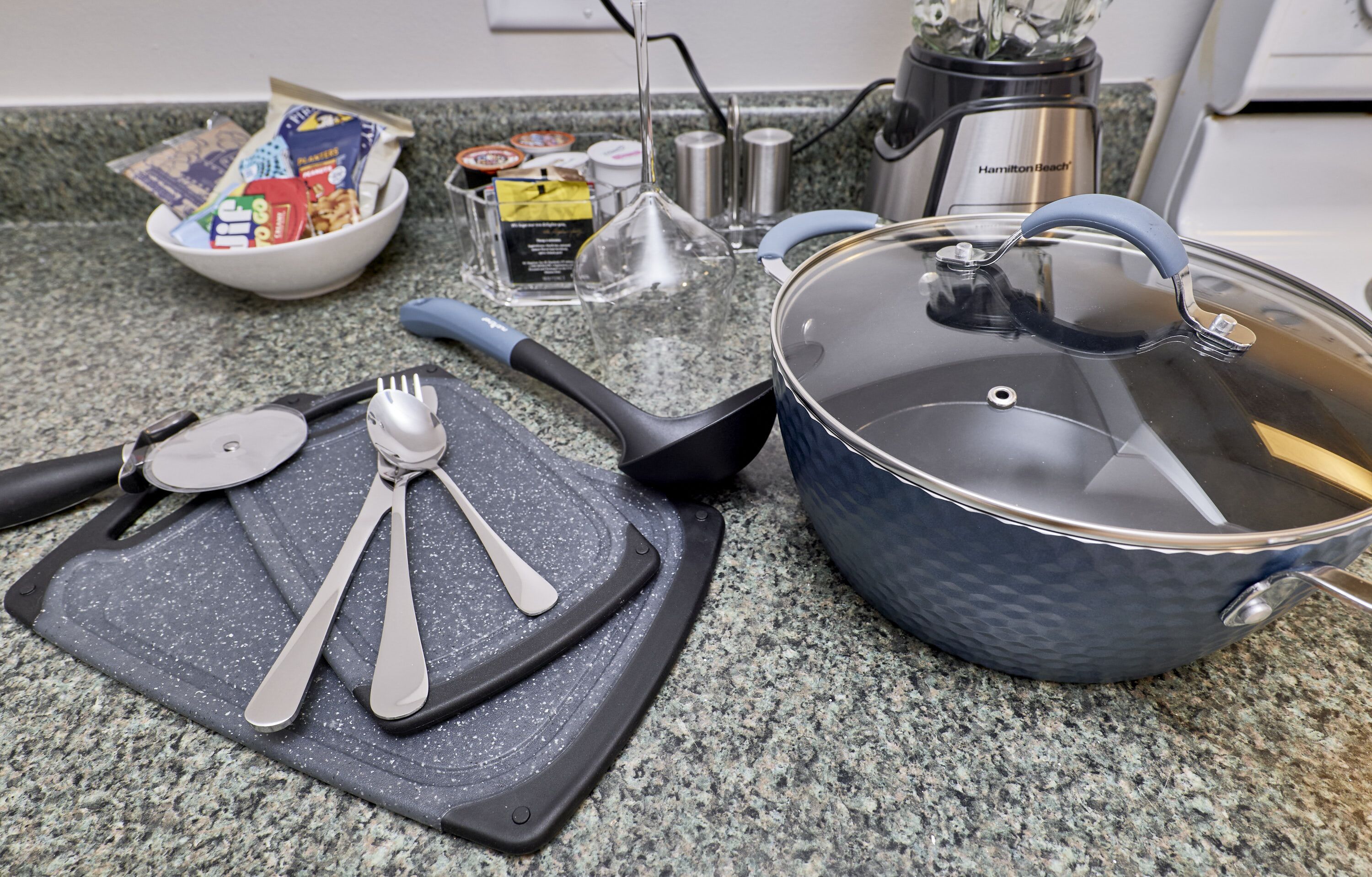 Una encimera de cocina con tabla de cortar, utensilios, una olla y un tazón de bocadillos.