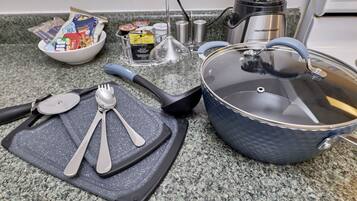 Una encimera de cocina con tabla de cortar, utensilios, una olla y un tazón de bocadillos.