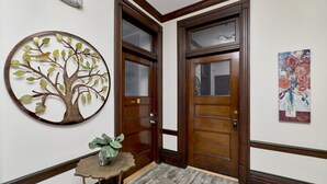 A hallway with wooden doors, a wall-mounted tree decoration, a small table with a plant, and a painting. -  White House at Grand Central (St. Louis)