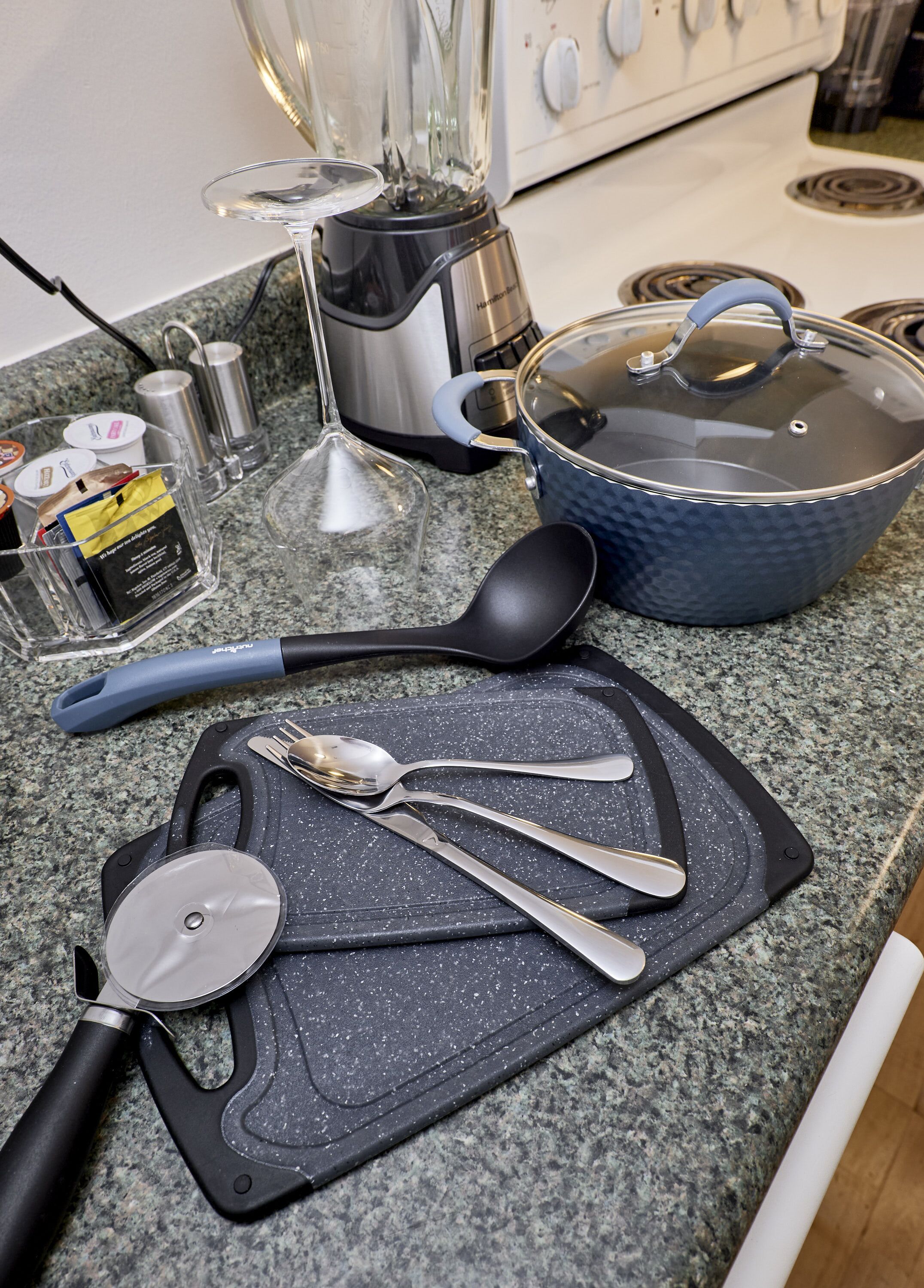 Eine Küchenarbeitsplatte mit Schneidebrett, Mixer, Topf, Löffel, Messer und Glas.