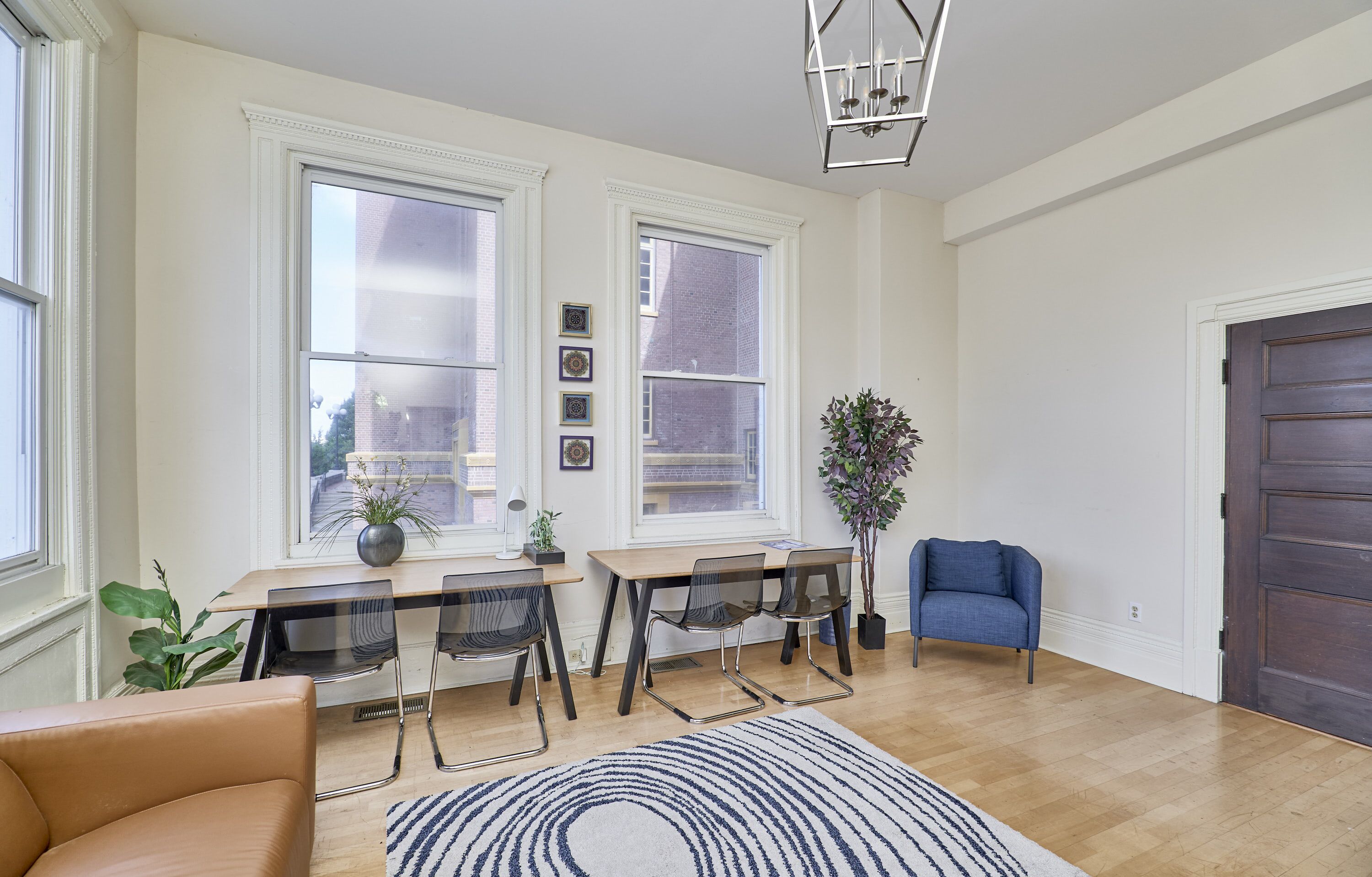 A modern living room with a wooden floor, a blue sofa, a dining table with chairs, and a large window with a view of buildings.
