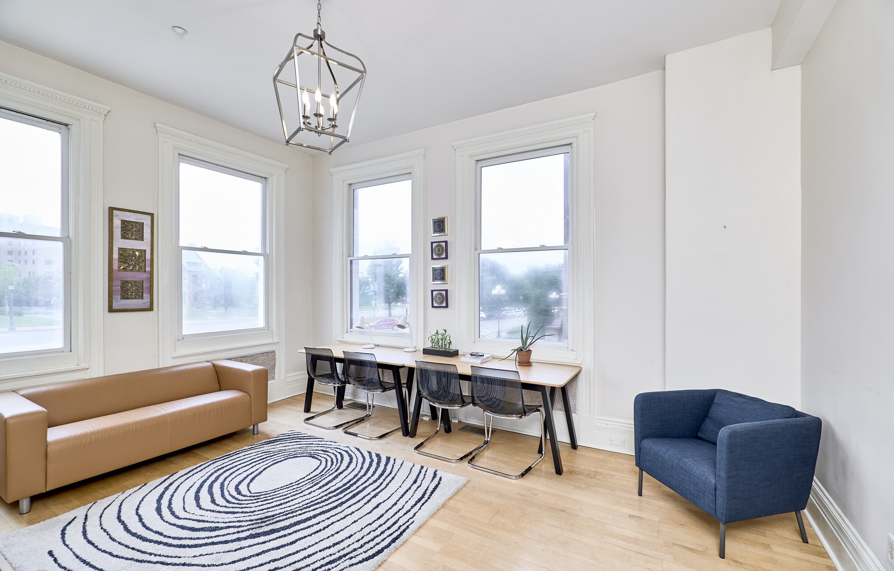 Una habitación amplia con un gran ventanal, un sofá, una mesa de comedor con sillas y un sillón azul.