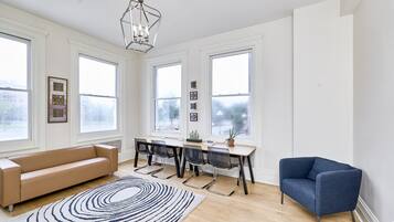 Una habitación amplia con un gran ventanal, un sofá, una mesa de comedor con sillas y un sillón azul.