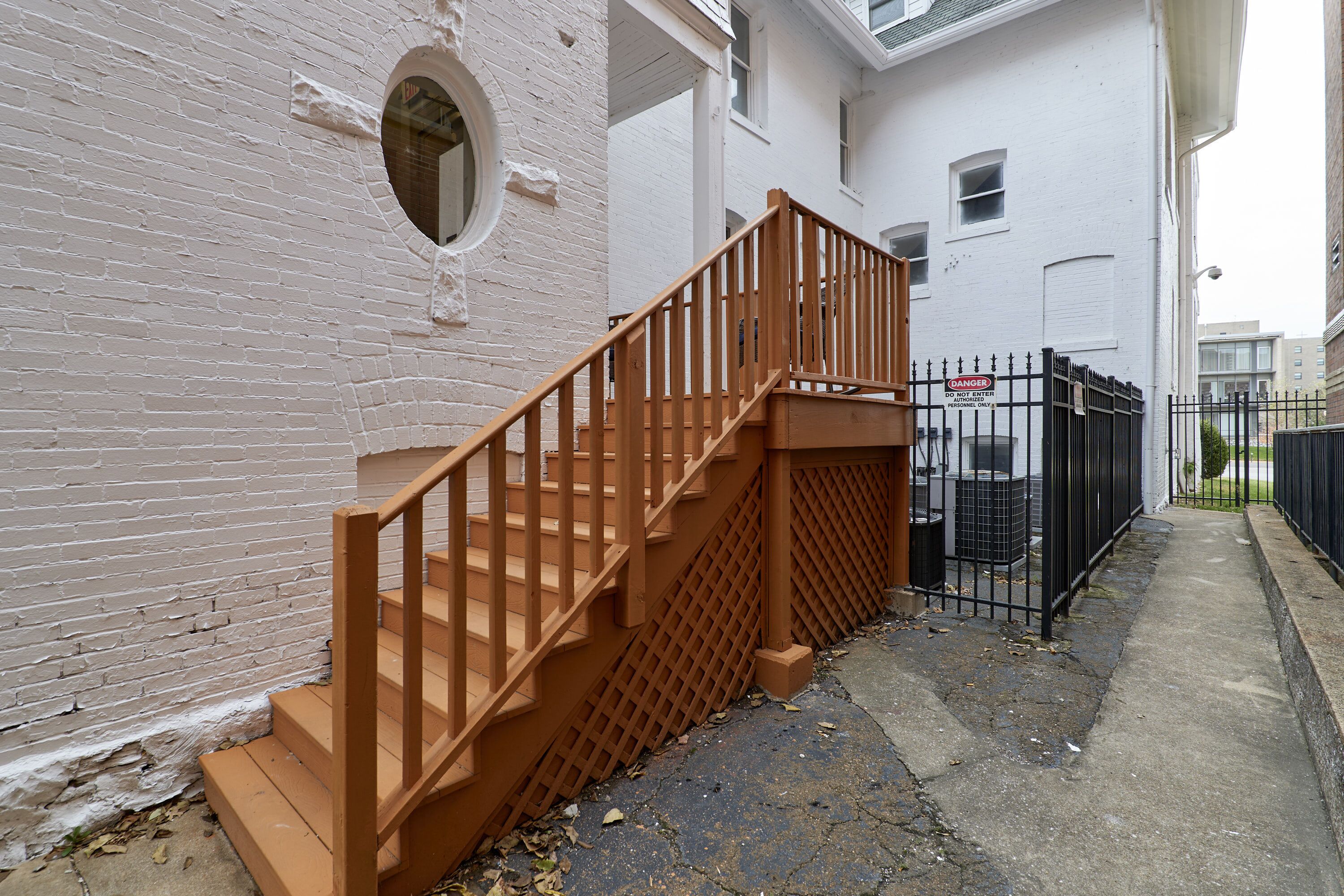 A staircase with wooden railings leading to a white building with a brick wall.