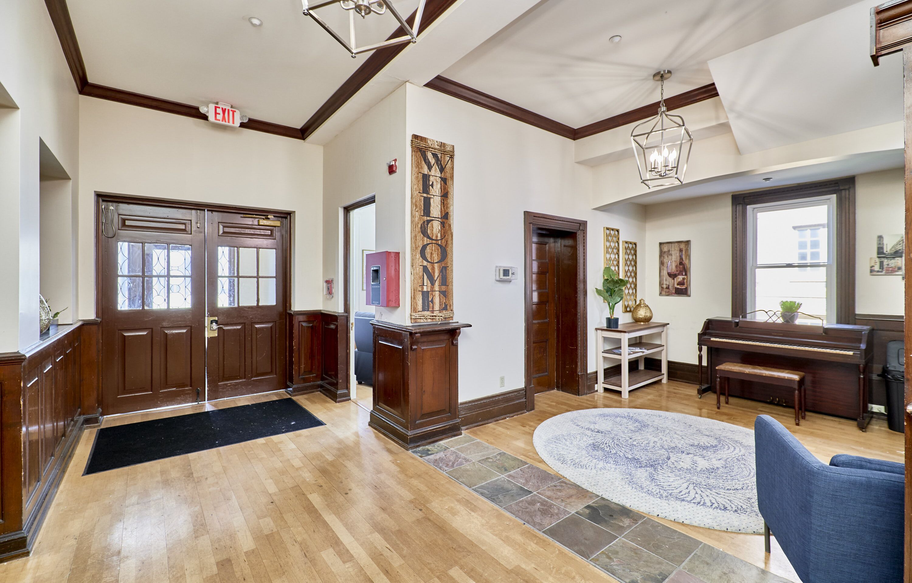 A spacious lobby with a grand piano, a welcome sign, and a large wooden door.