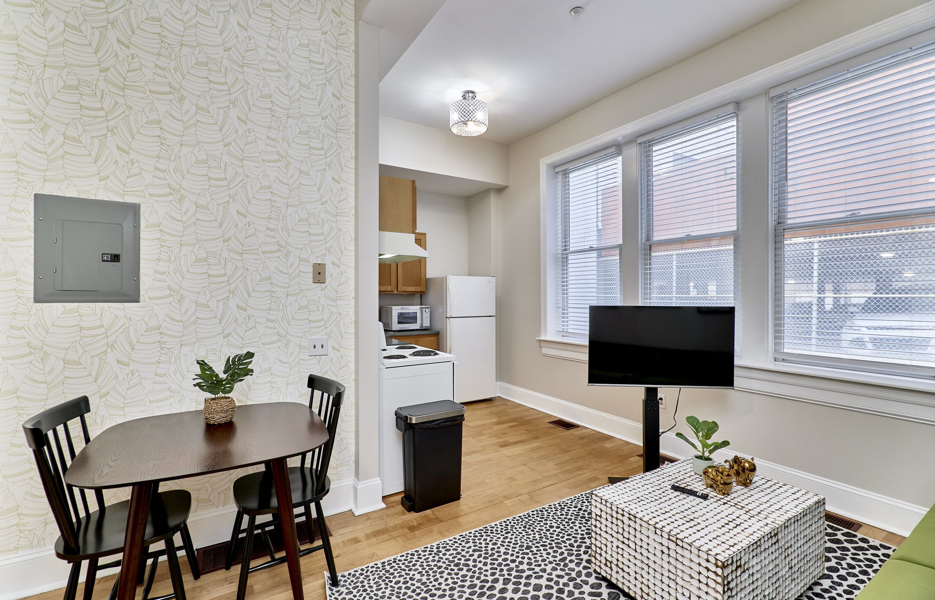 A modern kitchen with white appliances, a dining area with a wooden table and chairs, and a large window with blinds.