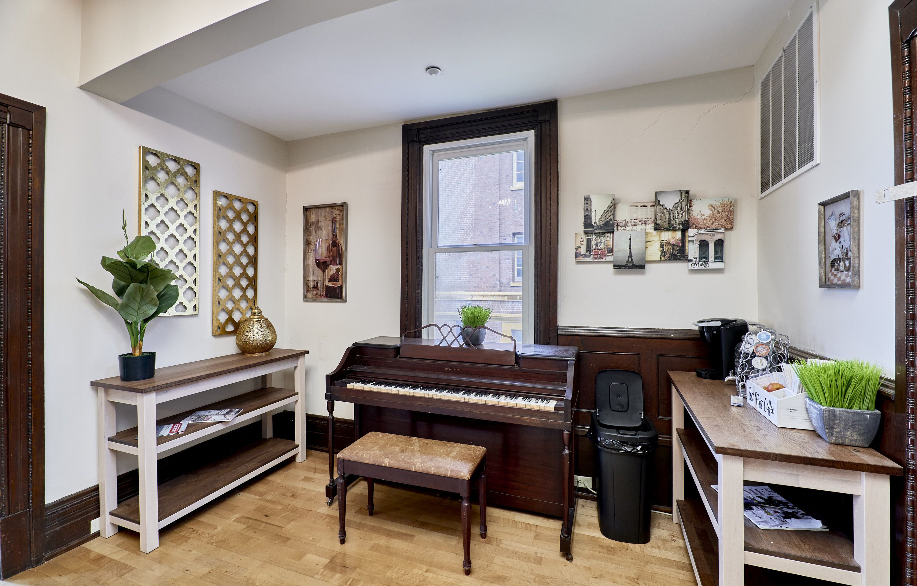 Un piano en una habitación con un banco de madera, una planta en maceta y obras de arte en las paredes.