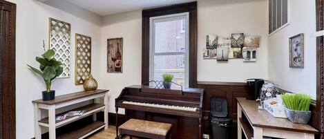 Un piano en una habitación con un banco de madera, una planta en maceta y obras de arte en las paredes.