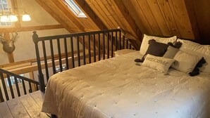 Une chambre confortable située dans les combles, avec un plafond en bois, un lit recouvert d’une literie blanche, une petite fenêtre et une tête de cerf décorative accrochée au mur.
