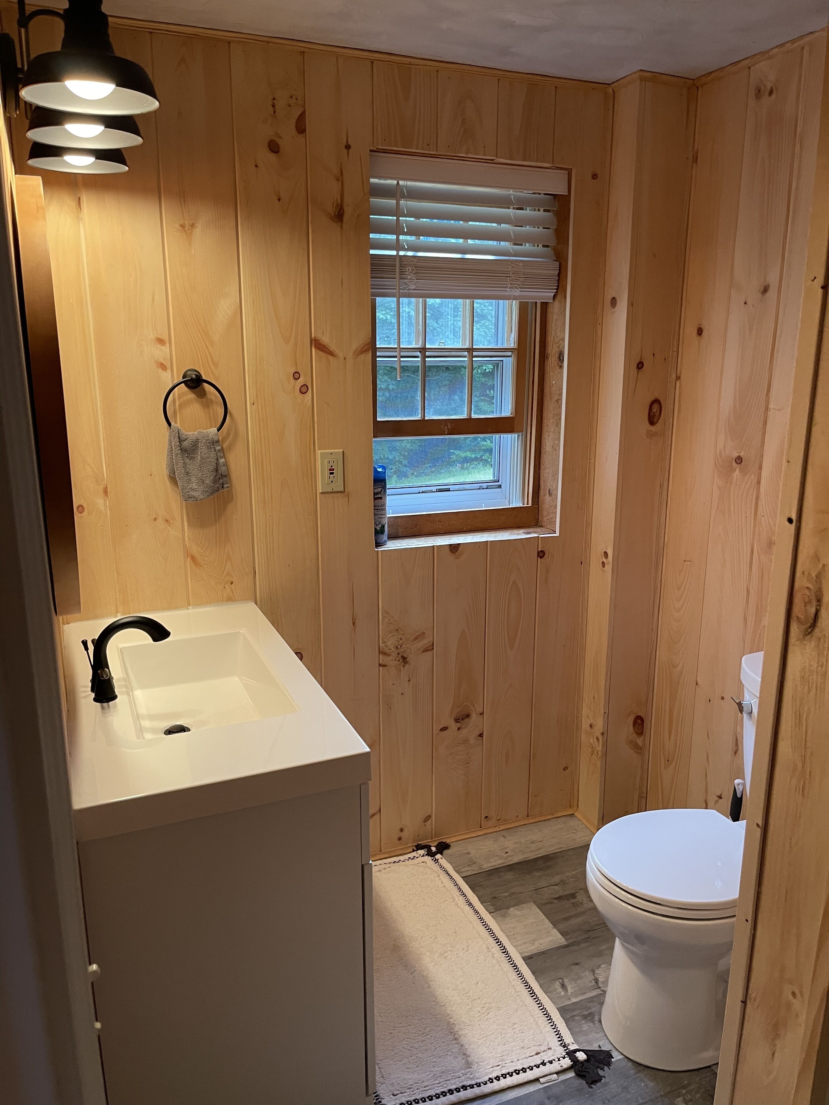 Een compacte badkamer met een witte wastafel, toilet en een raam met zonwering.