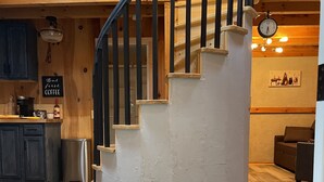 Un escalier en bois, une horloge, un coin cuisine et un salon avec un canapé.